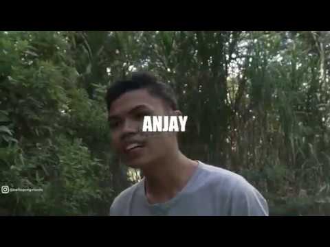 Pria muda berkaus abu-abu tersenyum di depan rumpun ilalang tinggi, dengan tulisan besar ANJAY di tengah gambar beresolusi rendah.