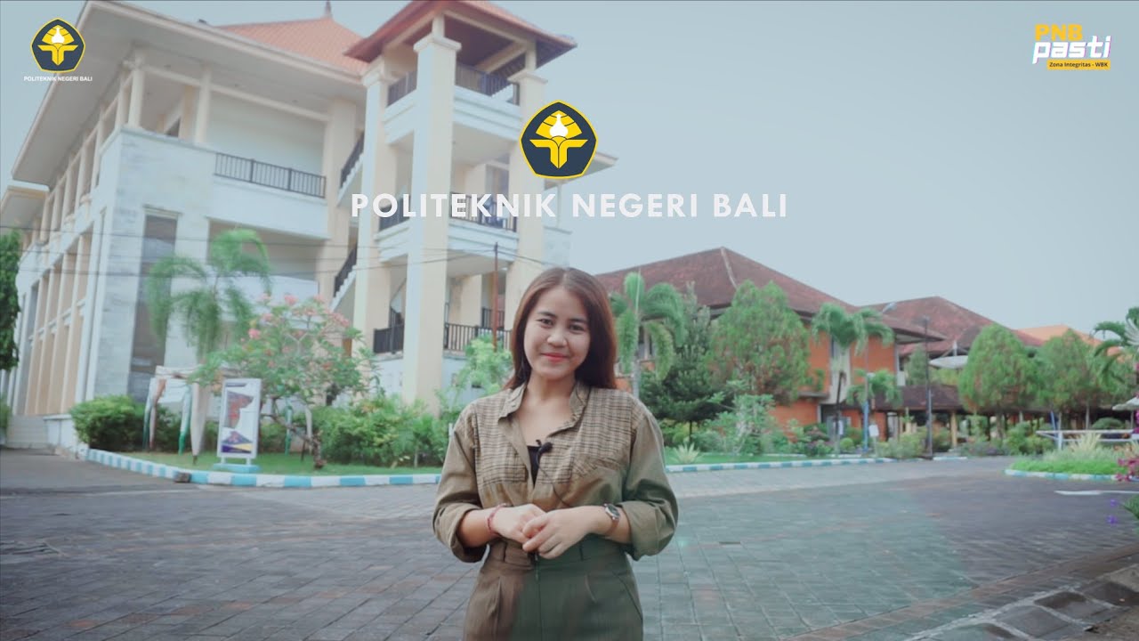 Perempuan berkemeja cokelat berdiri di halaman berpaving di depan gedung kampus putih beratap genteng merah pada siang hari.